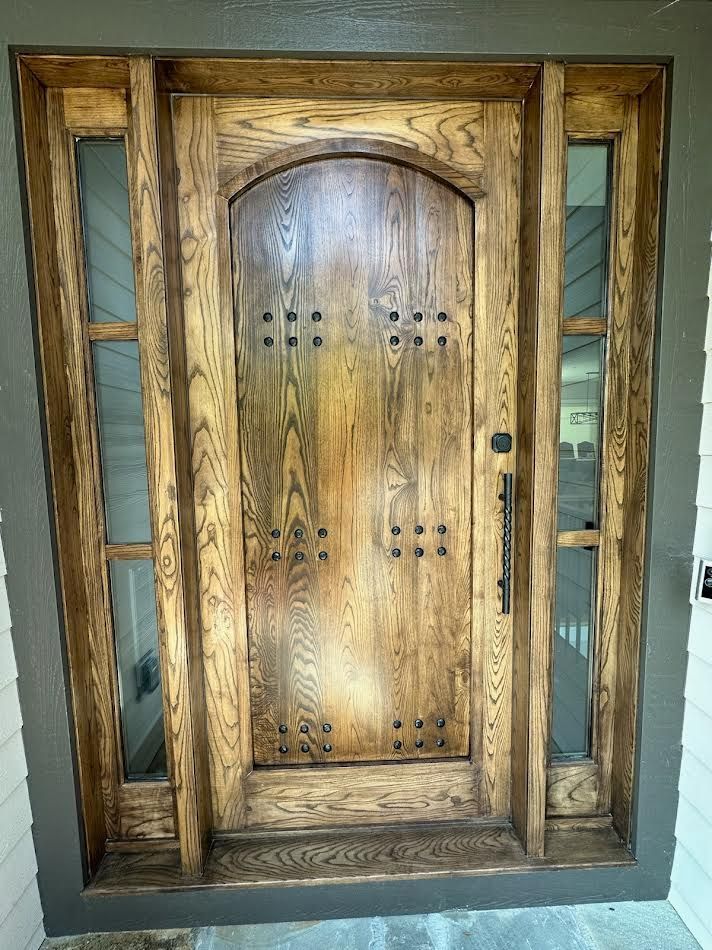 Wooden front door with sidelights, featuring decorative studs.