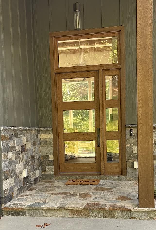 Wooden front door with glass panels on a stone porch. The door has a rectangular transom.