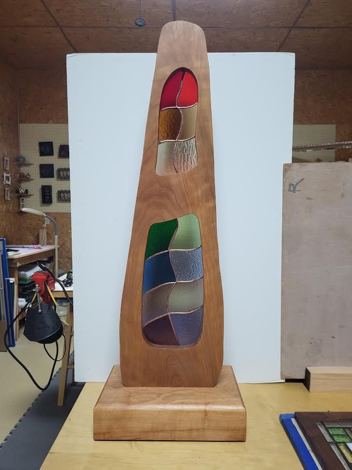 Wooden sculpture with inlaid stained glass sections of varying colors, on a wooden base.