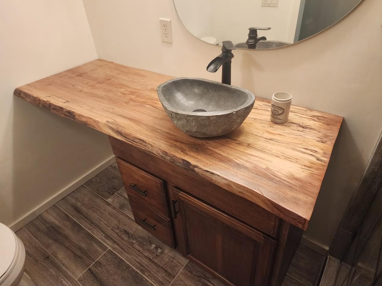 Bathroom vanity with a live-edge wooden countertop, stone sink, and dark faucet.