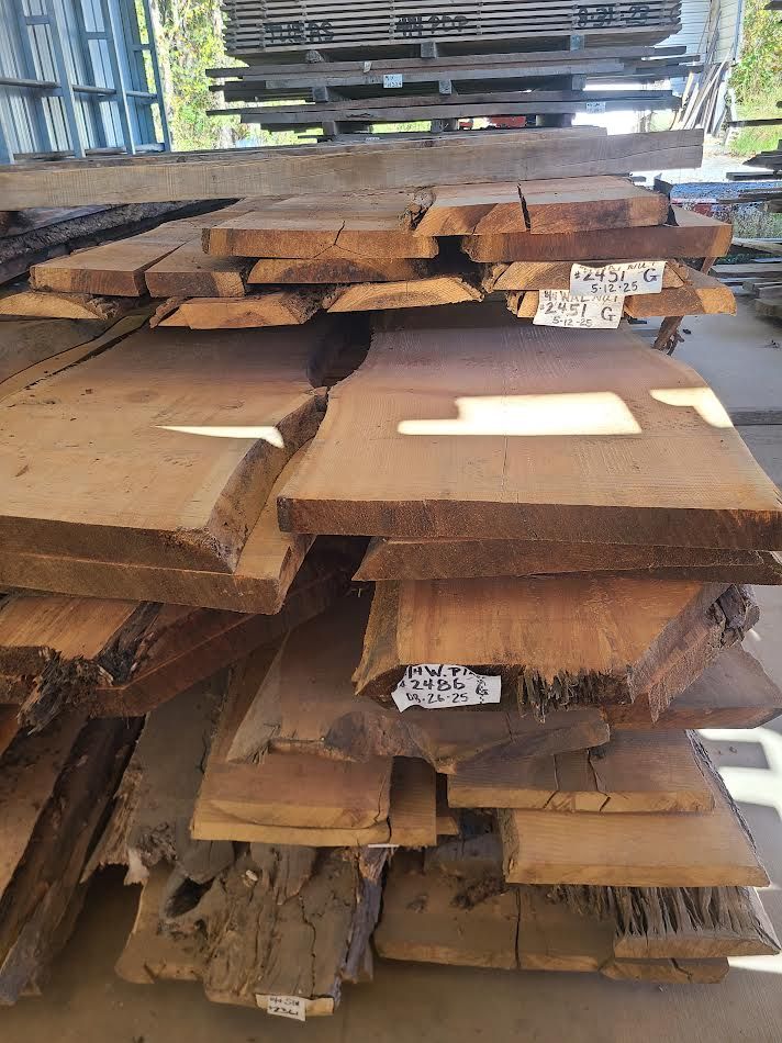 Pile of rough-cut lumber with natural edges, outdoors in a lumberyard, varying shades of brown.