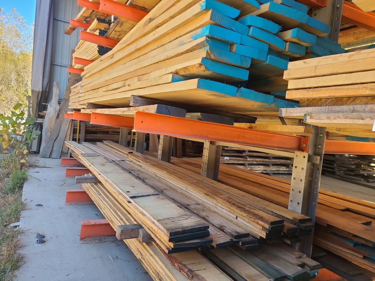 Stacks of lumber on orange metal racks, with blue-painted ends, outdoors.
