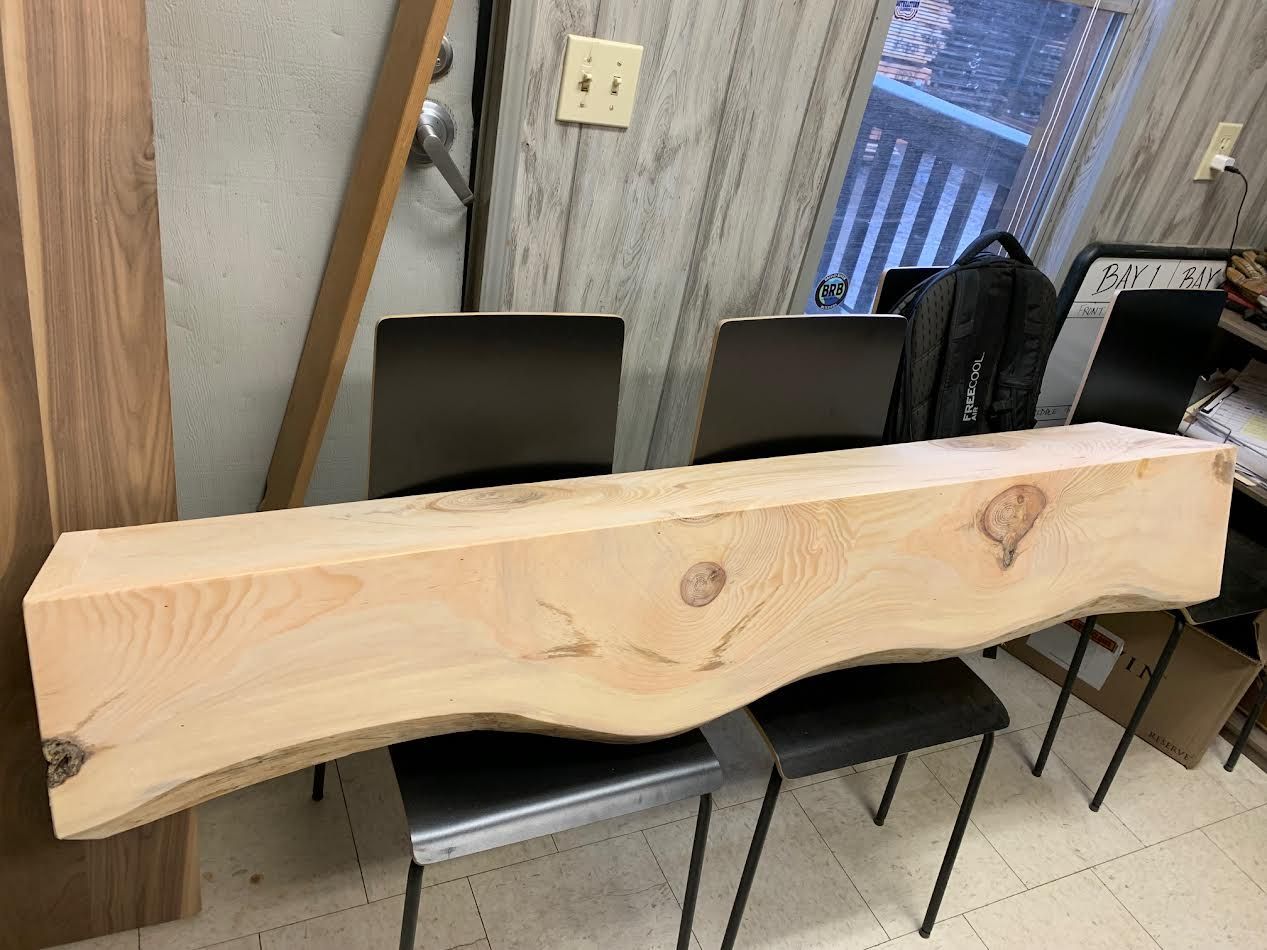 Wooden beam with a curved edge, resting on two chairs. Indoors, against a wall.