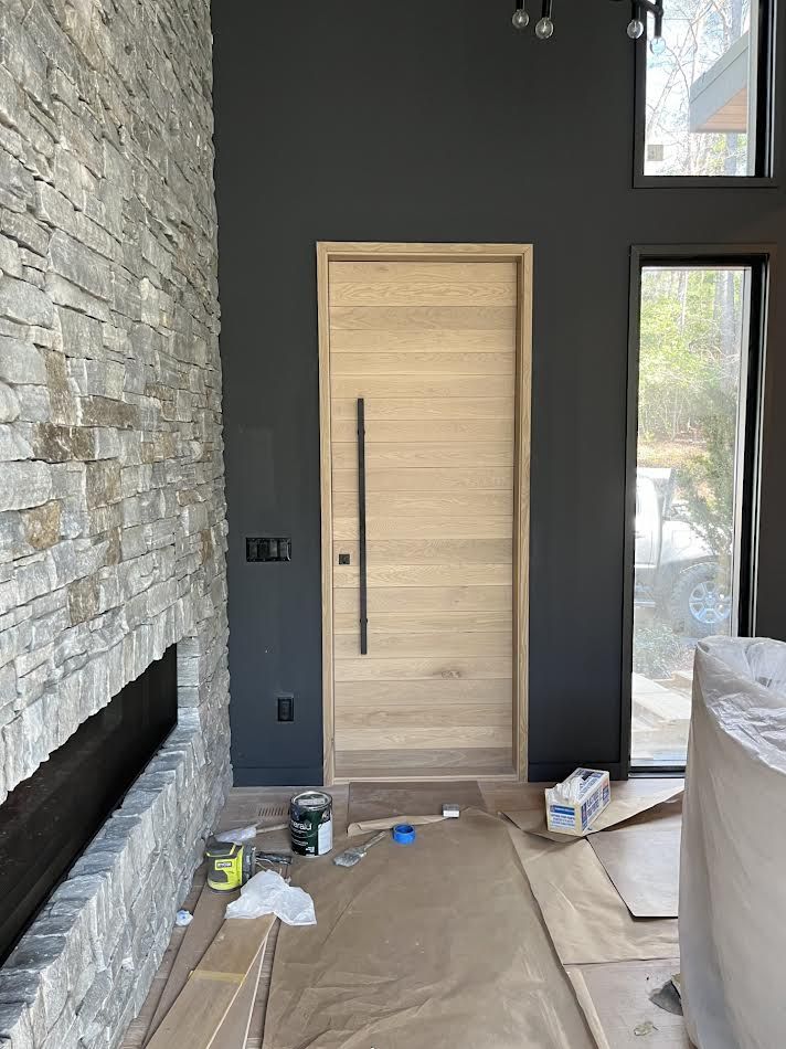 Entryway with light wood door, black handle, dark gray walls, and stone accent wall.