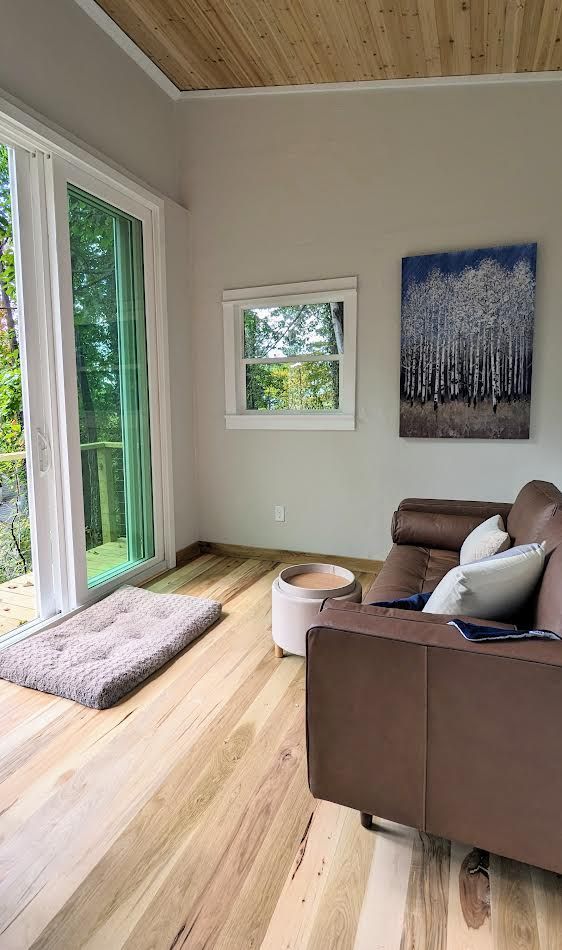 Living room with wood floors, large sliding glass door, brown sofa, and painting of trees.