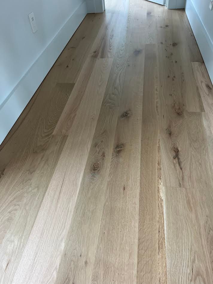 Light wood-plank flooring in a hallway with white baseboards and walls.
