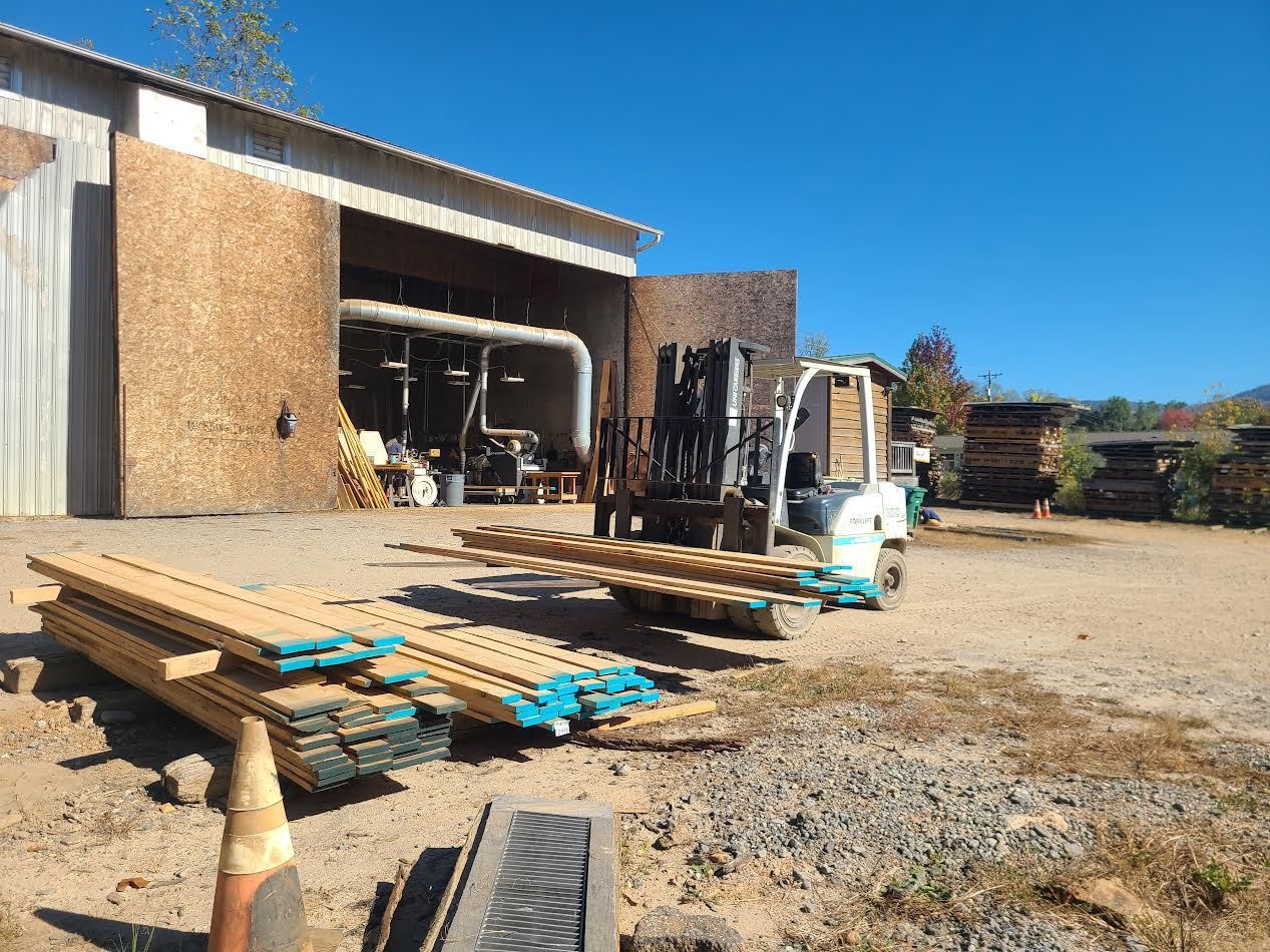 Forklift loading lumber outside a wooden building on a sunny day.