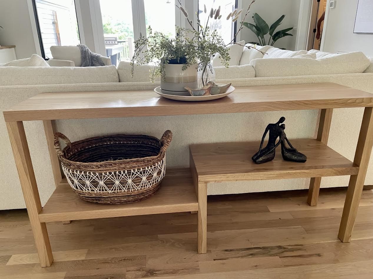 Wooden console table with a basket and shoes, set in front of a cream-colored couch.
