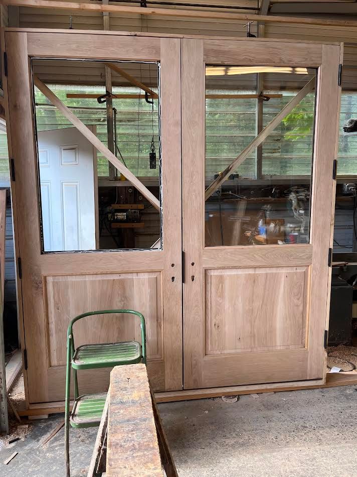 Two wooden doors with glass panels leaning against a wall in a workshop. A green chair sits in front.