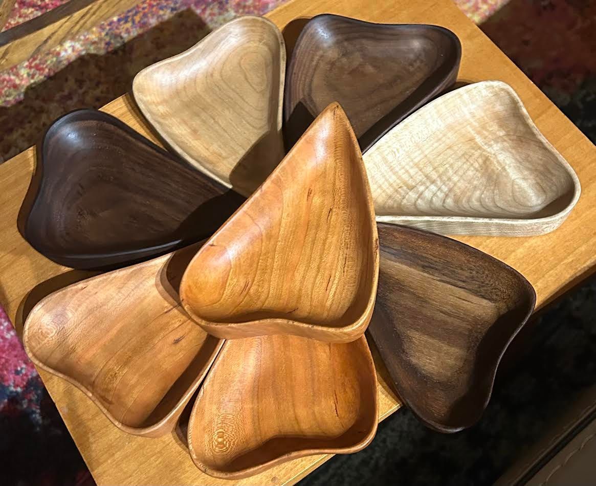 Seven handcrafted wooden heart-shaped bowls in varying wood tones.