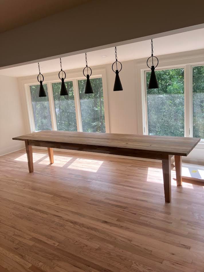 Long wooden dining table with black pendant lights, in front of a window.