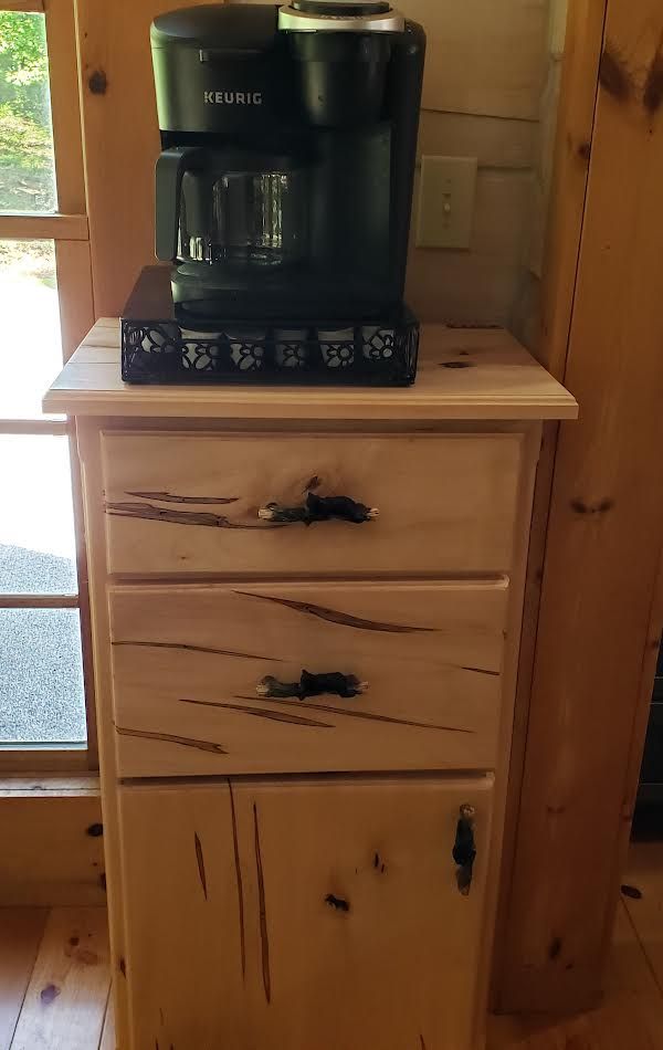 Coffee maker on a light wood cabinet with drawers and a door, inside a room.