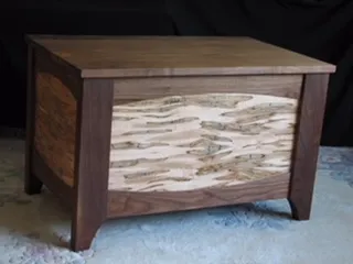Wooden chest with a light-colored, patterned front panel and a dark wood frame.