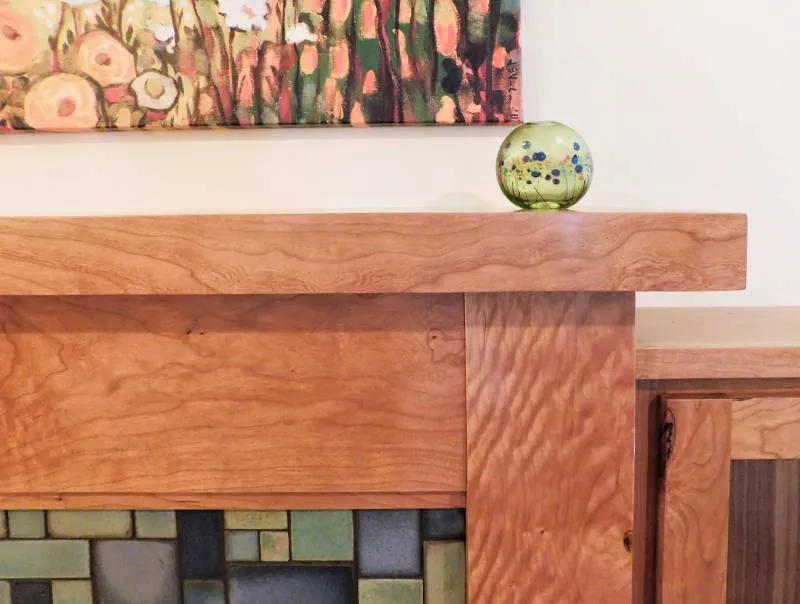 Wooden mantel with a glass orb, mosaic tiles, and a colorful abstract painting.
