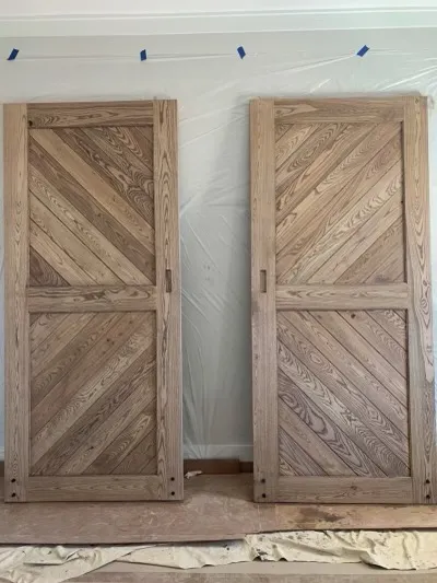 Two wooden doors with angled planks lean against a wall, partially taped, ready for installation.