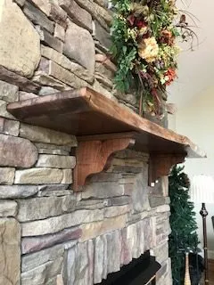 A wooden shelf on a stone fireplace. A floral arrangement sits above the shelf.