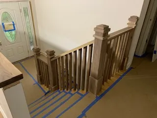 Staircase with wooden balusters and newel posts in a home's entryway. Cardboard covers the floor.