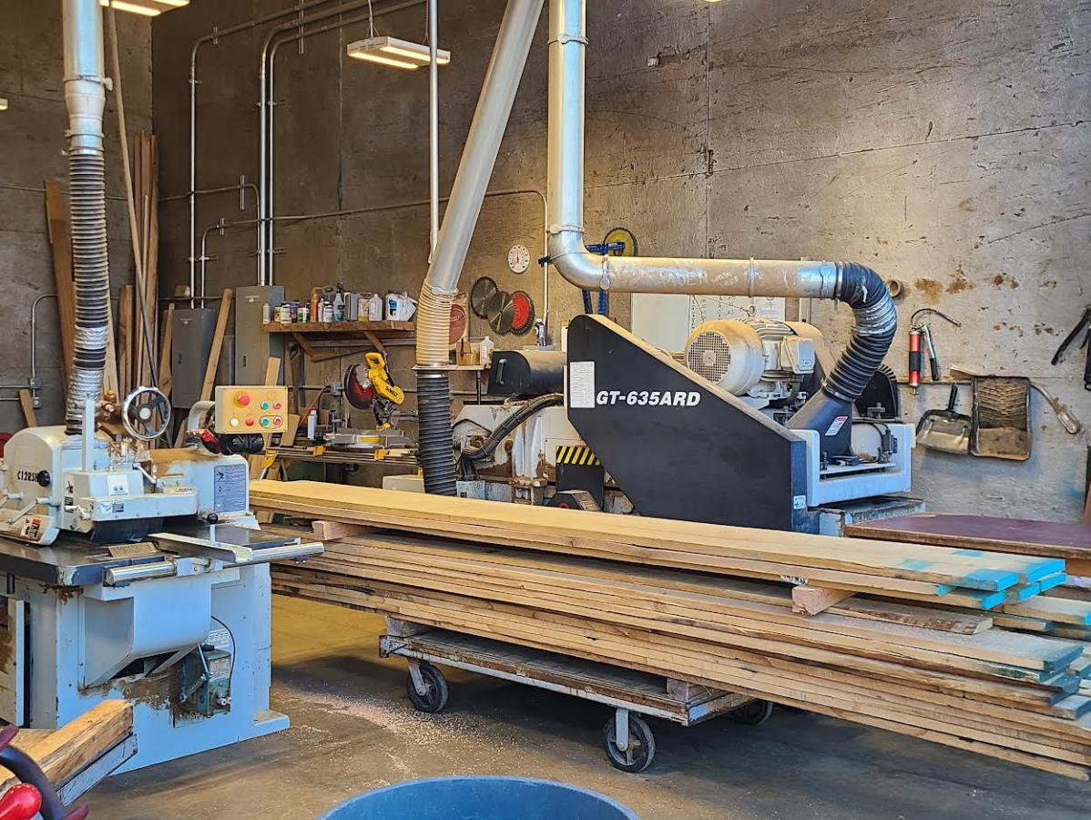 Woodworking shop with stacked lumber on a cart, table saw, and dust collection system.