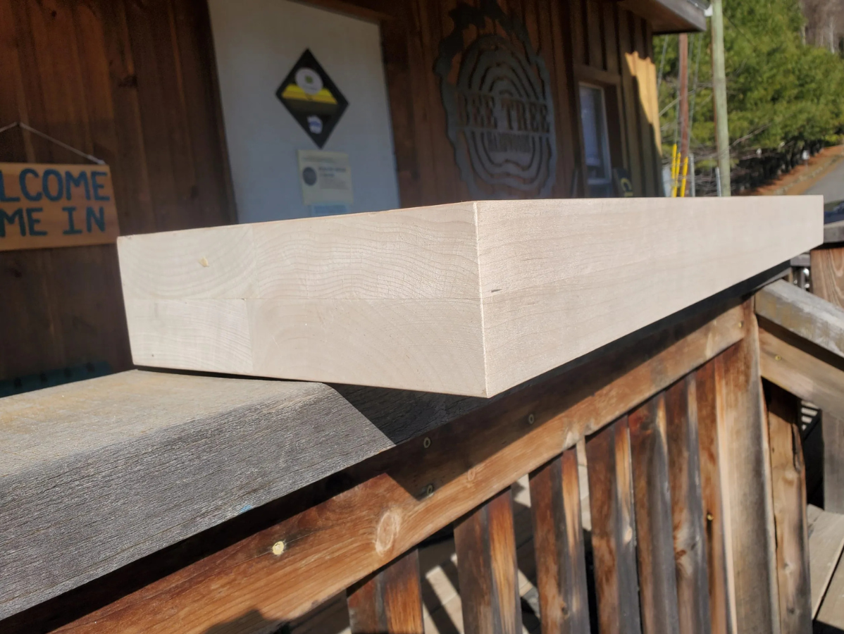 Cream-colored rectangular beam on a wooden porch railing, near a rustic building with signage.