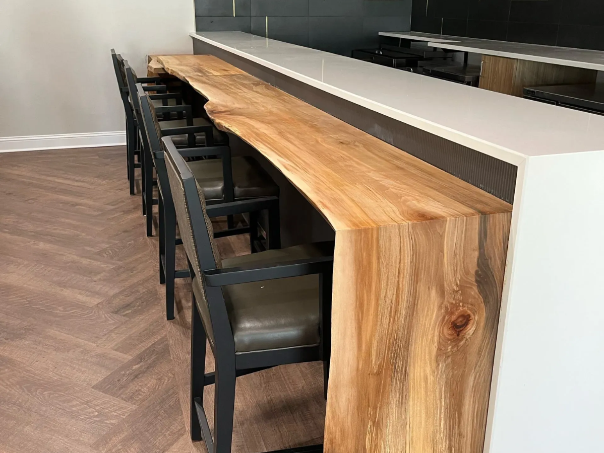 Wooden bar with a live edge, black metal bar stools, and a white countertop.