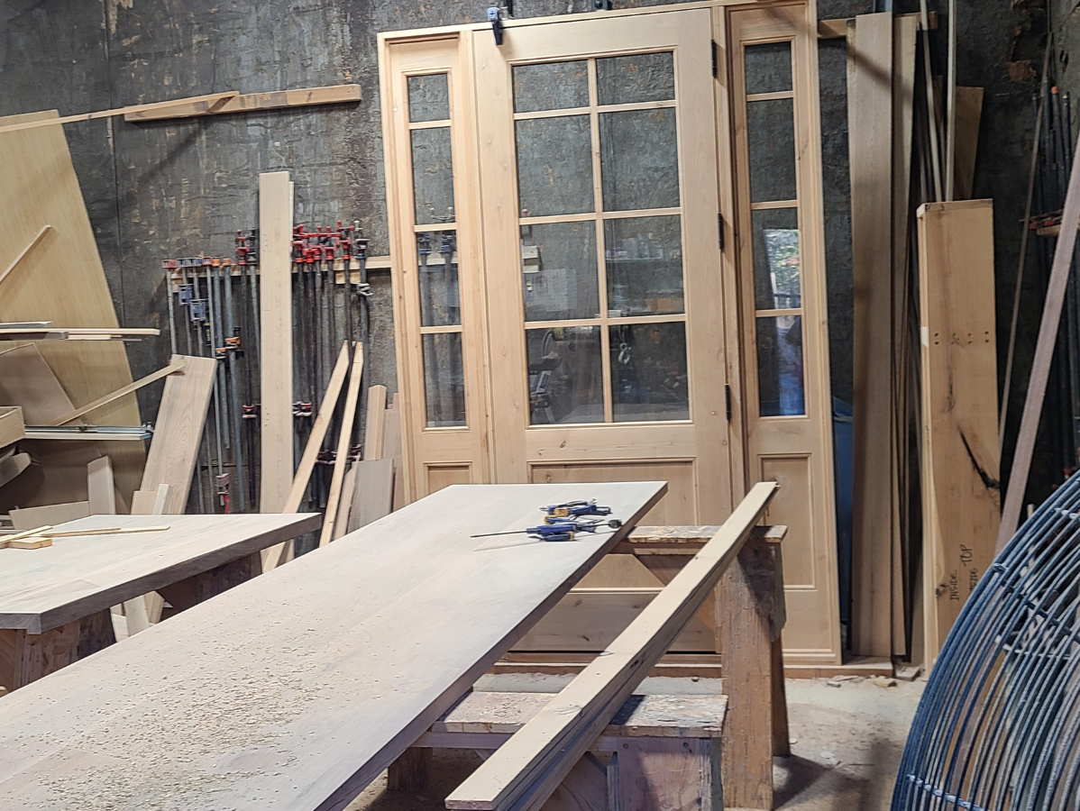 Workshop with wooden doors and table; tools and lumber visible.