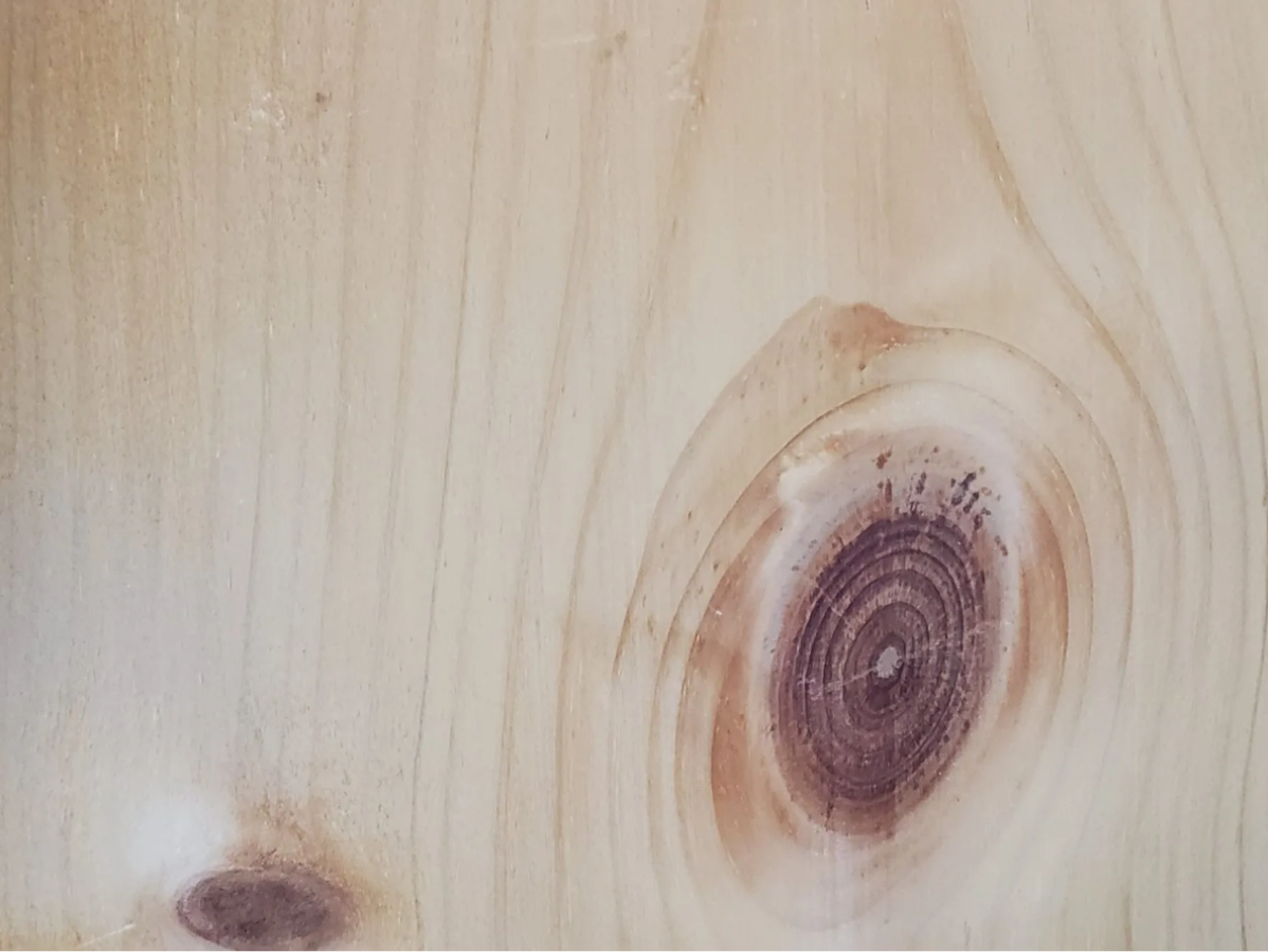 Close-up of light-colored wood grain with a large, reddish-brown knot and smaller knots.