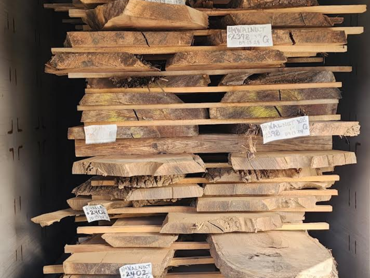 Stack of rough-cut wood slabs, separated by thin wooden supports, inside a kiln.
