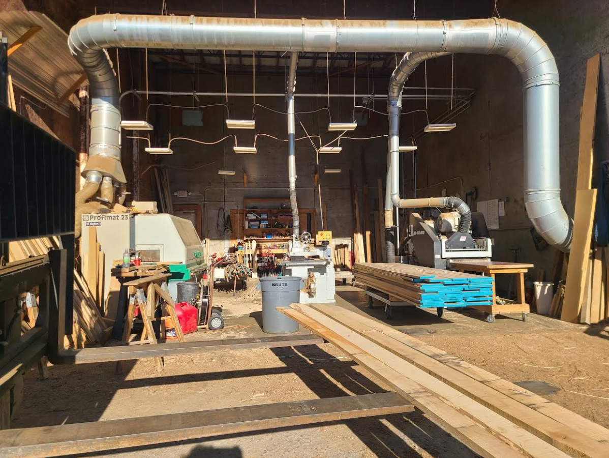 Woodworking shop interior with ductwork, saws, lumber, and tools.