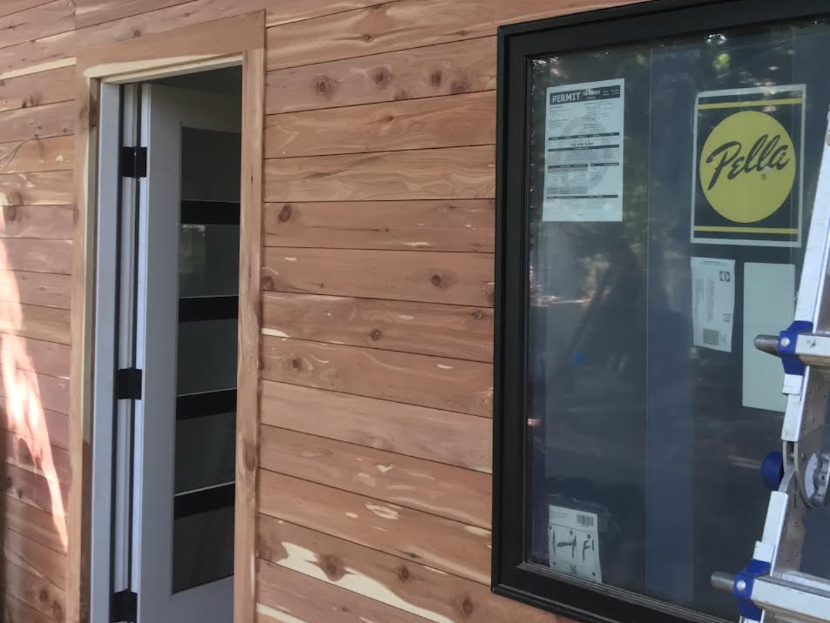 Exterior wall with open door and window, horizontal cedar siding. Door is gray, window frame is black.