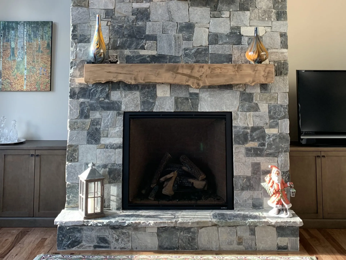 Stone fireplace with wooden mantle, decorations, and a lit fire.
