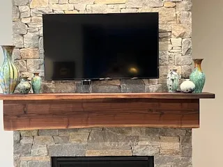 Television above a wooden mantle with decorative vases on a stone fireplace.