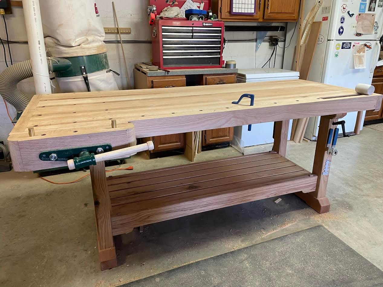 A wooden workbench with a vise, a lower shelf, and a tool chest in the background.