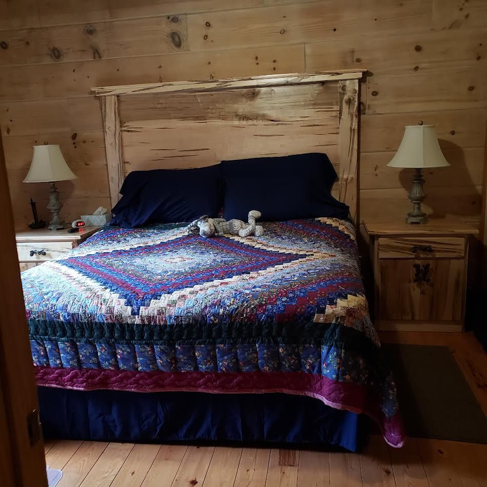Bedroom with wood paneling, a bed with a quilt, nightstands, and lamps.