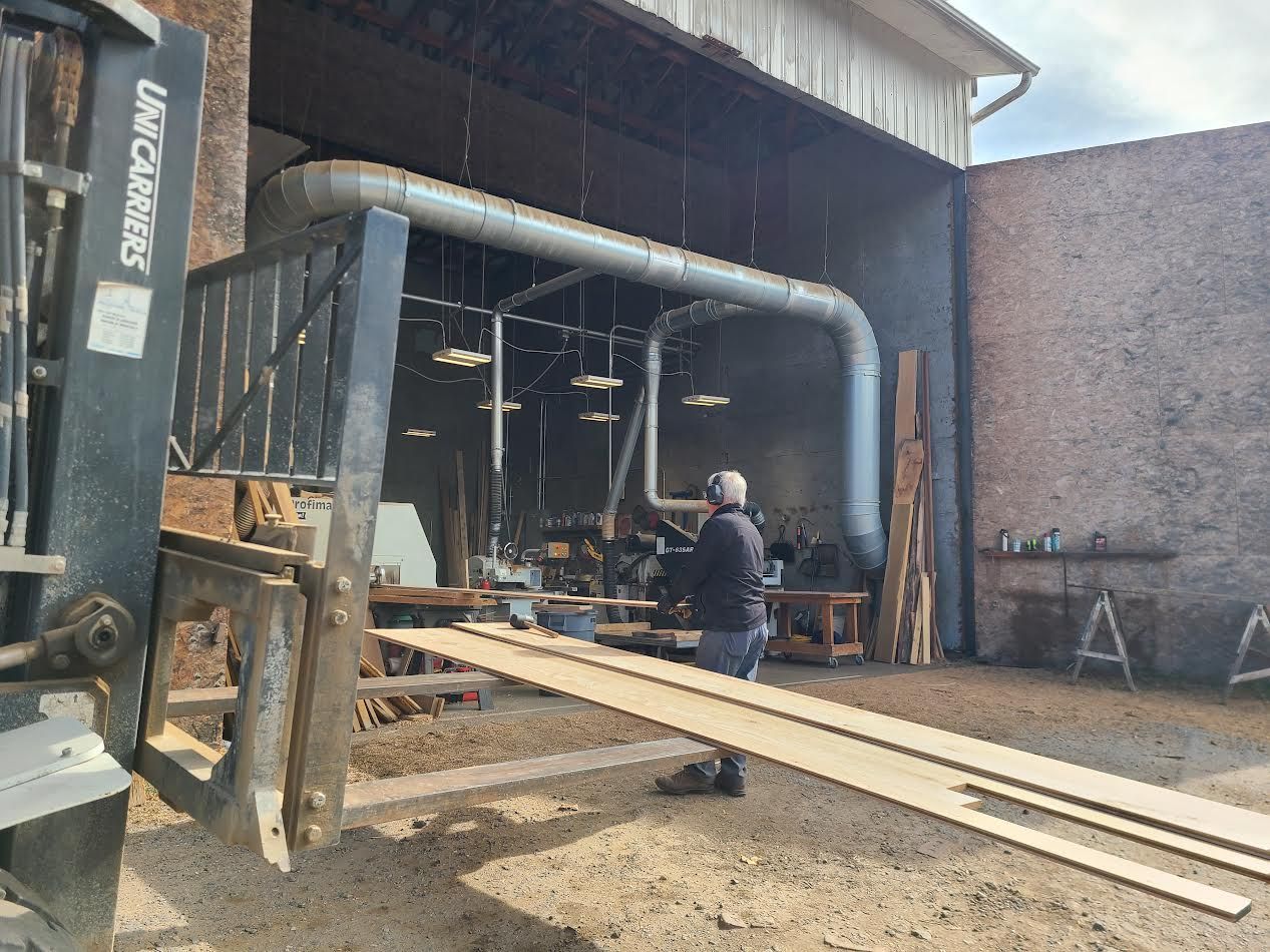 Forklift with wood planks, man in a shop loading into a machine.