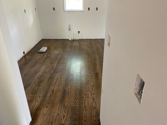 Room with dark wooden floor, white walls, electrical outlets, and a small window.