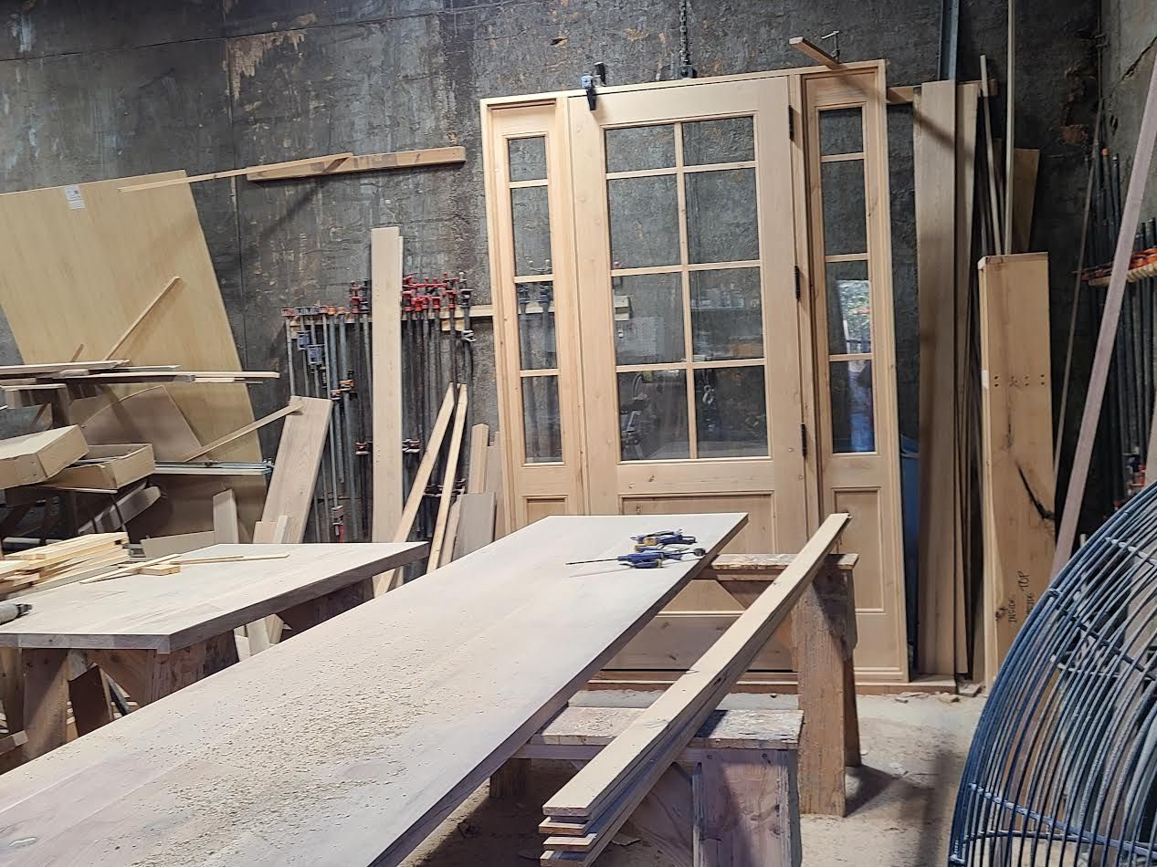 Workshop interior with wooden doors, a long workbench covered in sawdust, and various tools.