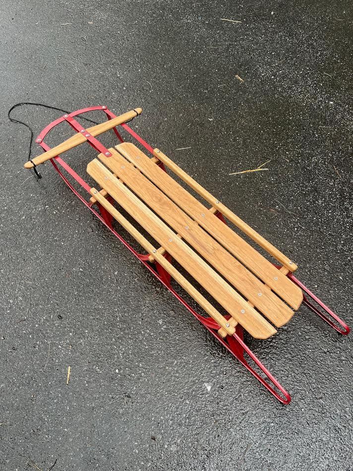 Red and wood sled on wet asphalt. Black rope attached to front.