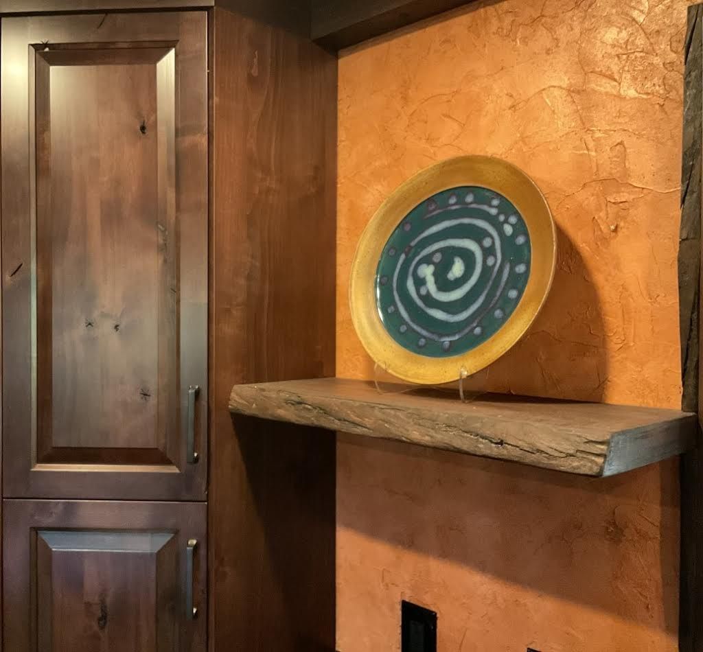 Wooden cabinets beside an orange textured wall with a stone shelf and decorative plate.