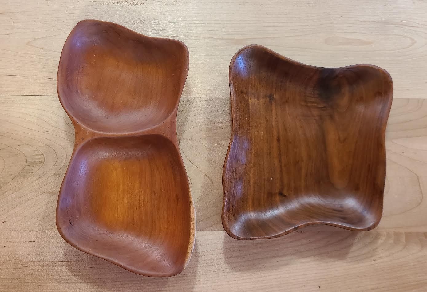 Two wooden, irregularly shaped bowls on a wood surface. One bowl has two connected sections.