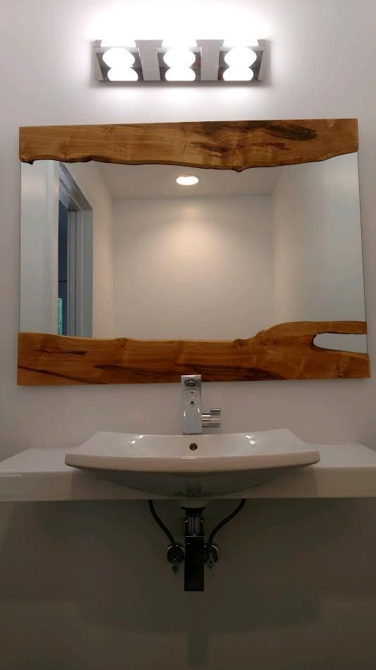 Bathroom vanity with a live-edge wooden mirror frame, white sink, and light fixture above.