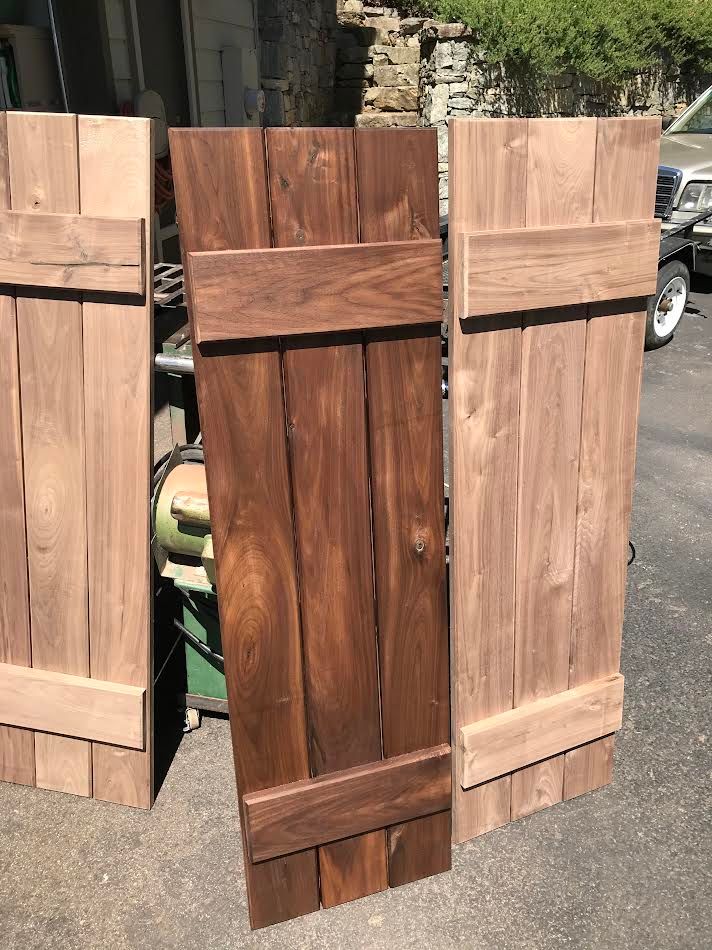 Three wooden shutters of varying stain colors leaning against a surface.