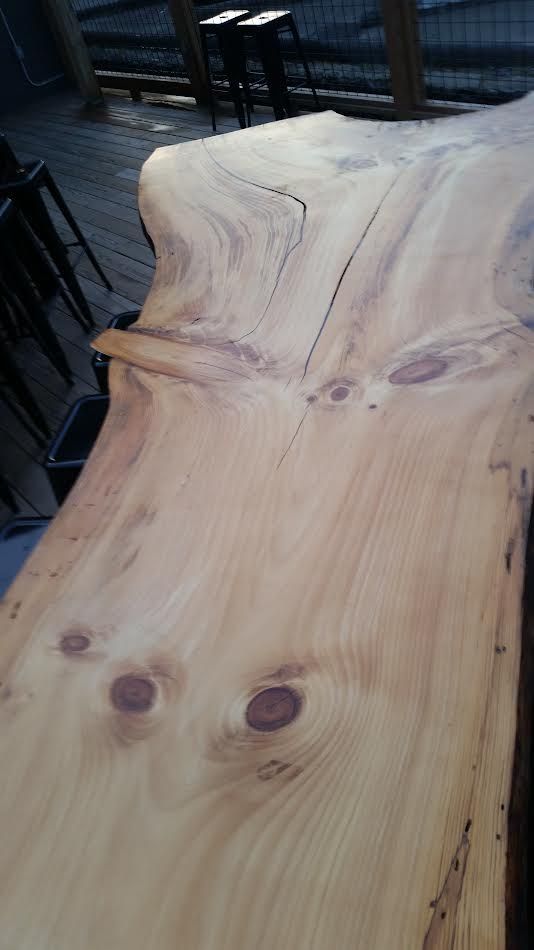 Close-up of a light-colored, rustic wooden table with natural edge and dark spots.