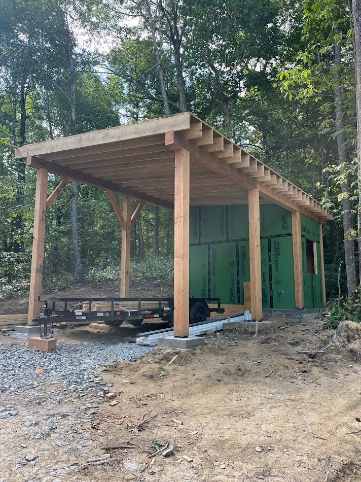 A partially-built wooden shed with a green-walled storage area and an open-sided roof, a trailer is parked inside.