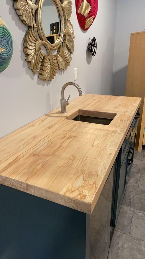 Wooden countertop with sink, faucet, and blue cabinet in room with decorative wall art.