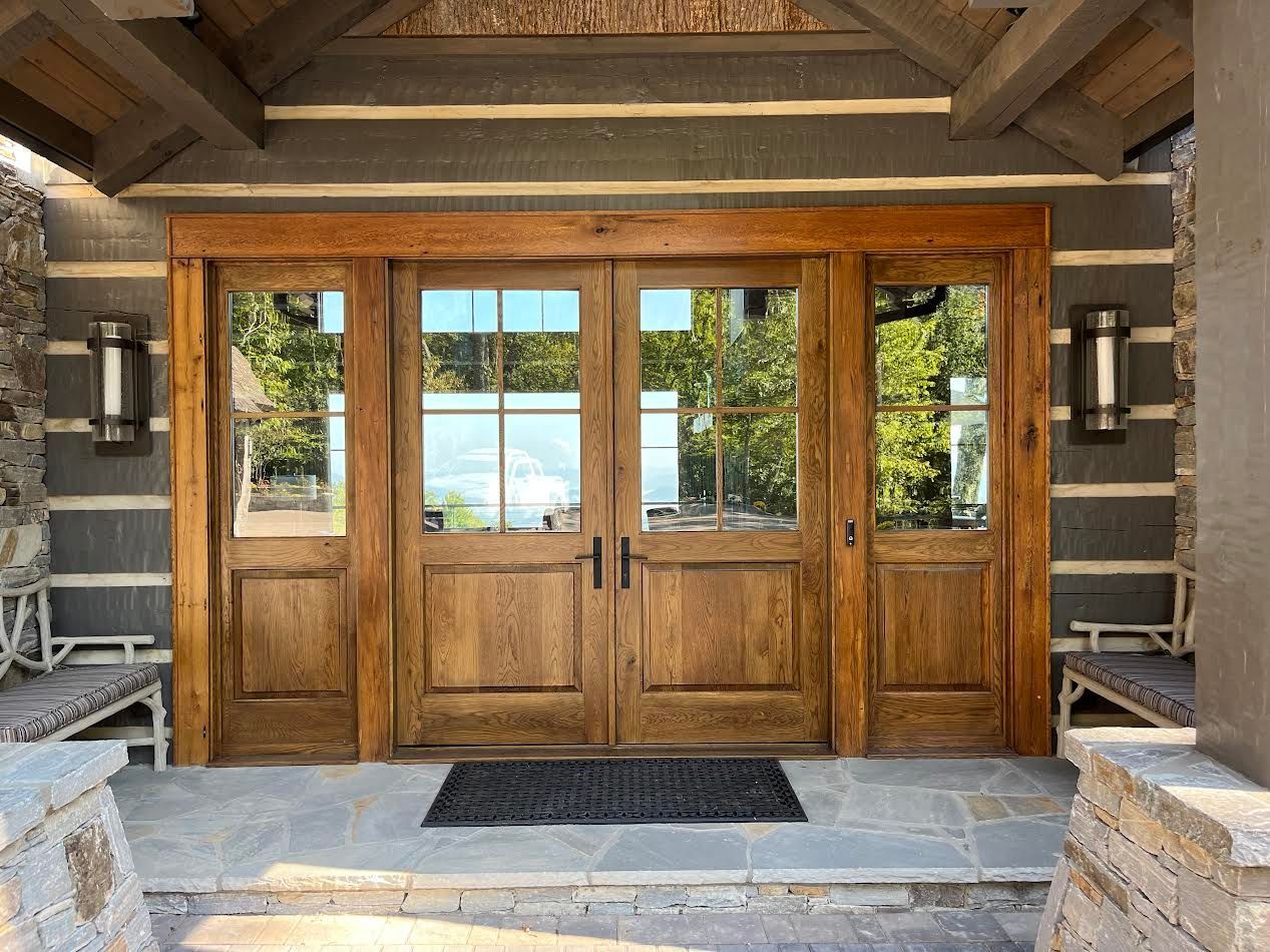 Wooden double doors with glass panels and sidelights on a stone porch.