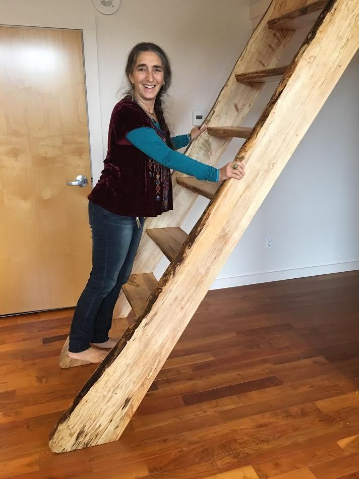 Woman smiling, holding railing, ascending rustic wooden stairs. Interior with wood floor and a door.