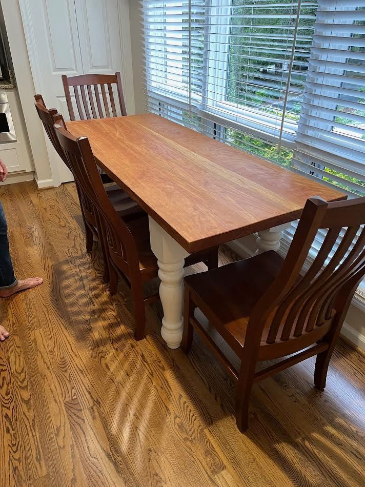 Dining table with four chairs on hardwood floor near a window. Tabletop is wood with white legs.