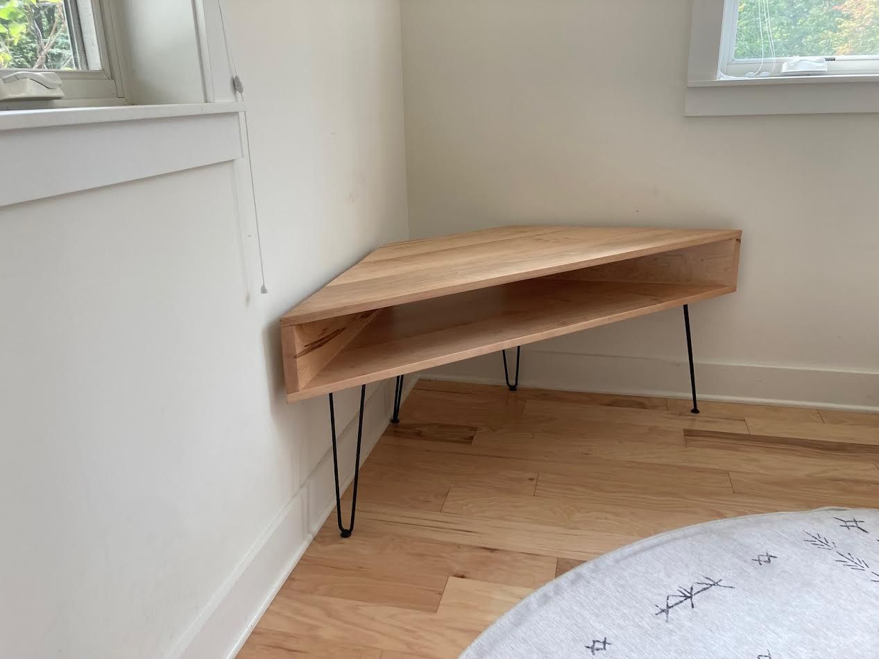 Triangular wooden corner shelf with hairpin legs, next to a window.