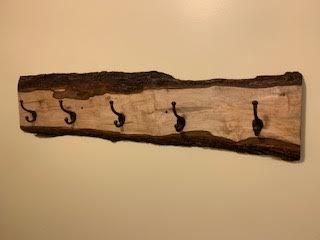 Wooden coat rack with five black metal hooks mounted on a beige wall.