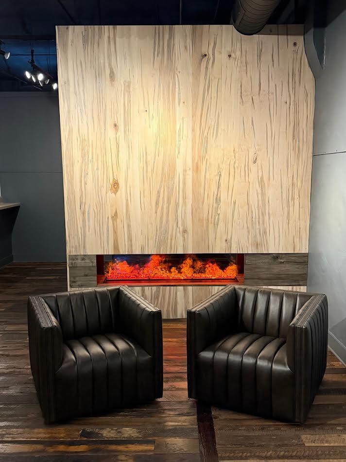 Two black leather chairs face a modern fireplace with a light wood backdrop.
